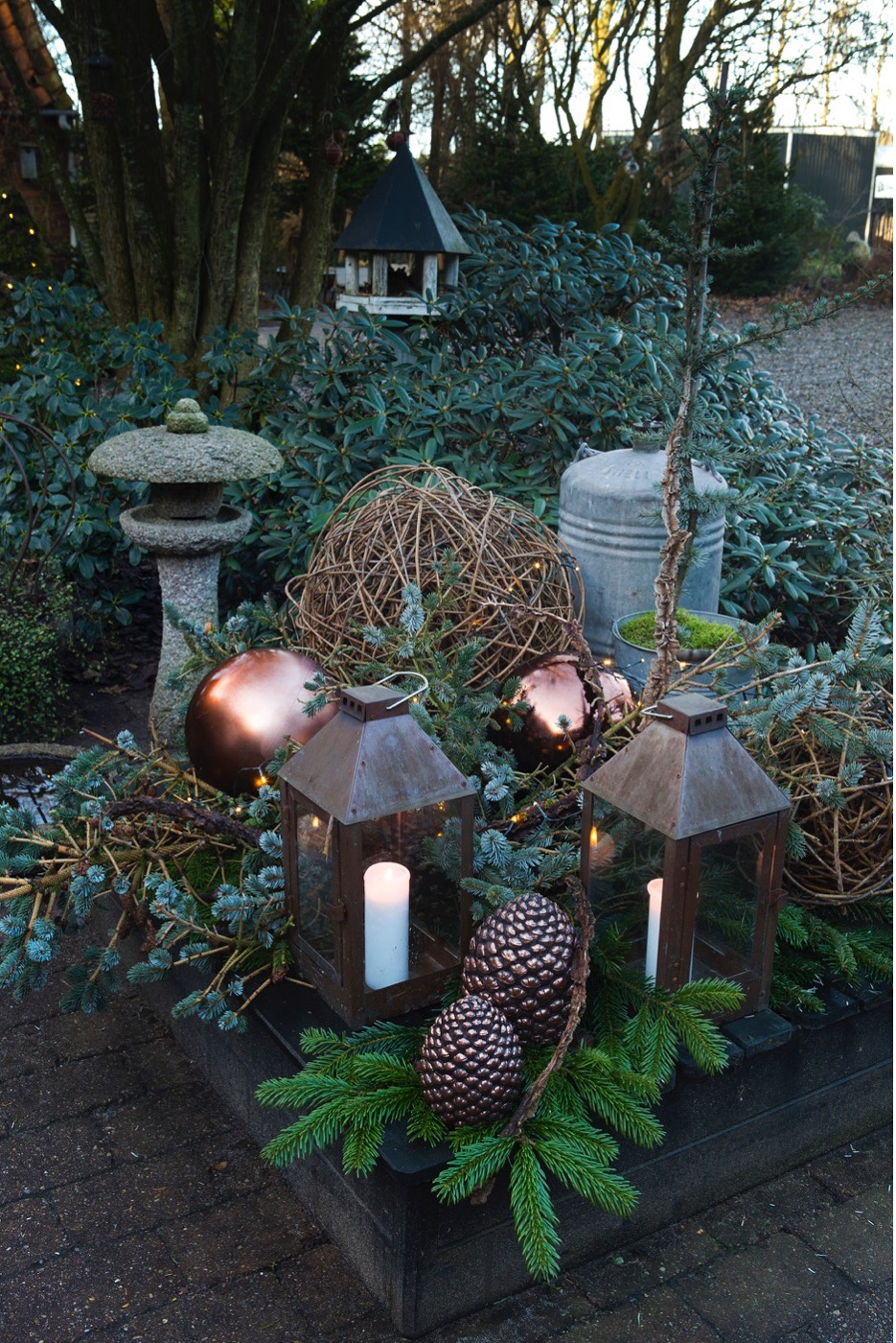 Et juletableau i Fru Pedersens have med forskellig gran samt grene fra korkelm, som får selskab af store lanterner af kobber, kobberkogler og store, kobberfarvede plastikkugler. Foto Ann Malmgren