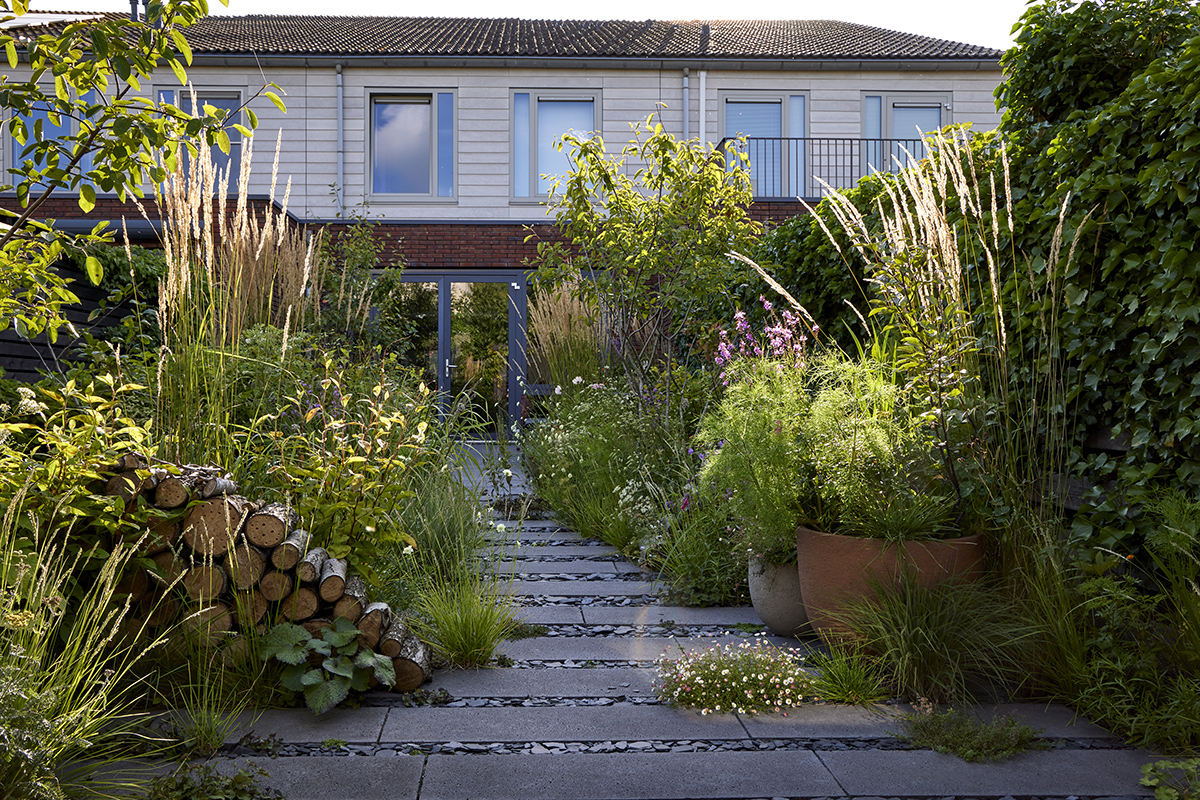 Haven er designet, så beboerne kunne se ud på en interessant beplantning året rundt. Designer Stefano Martinez har skabt højde med 3 bærmispler placeret rundt i haven. De høje græsser Calamagrostis x acutiflora 'Karl Foerster' tager opmærksomheden i sensommerens bede. Stramme, lave brændestabler giver levesteder til smådyr, men fungerer designmæssigt som skulpturelle elementer. Foto: Alister Thorpe.