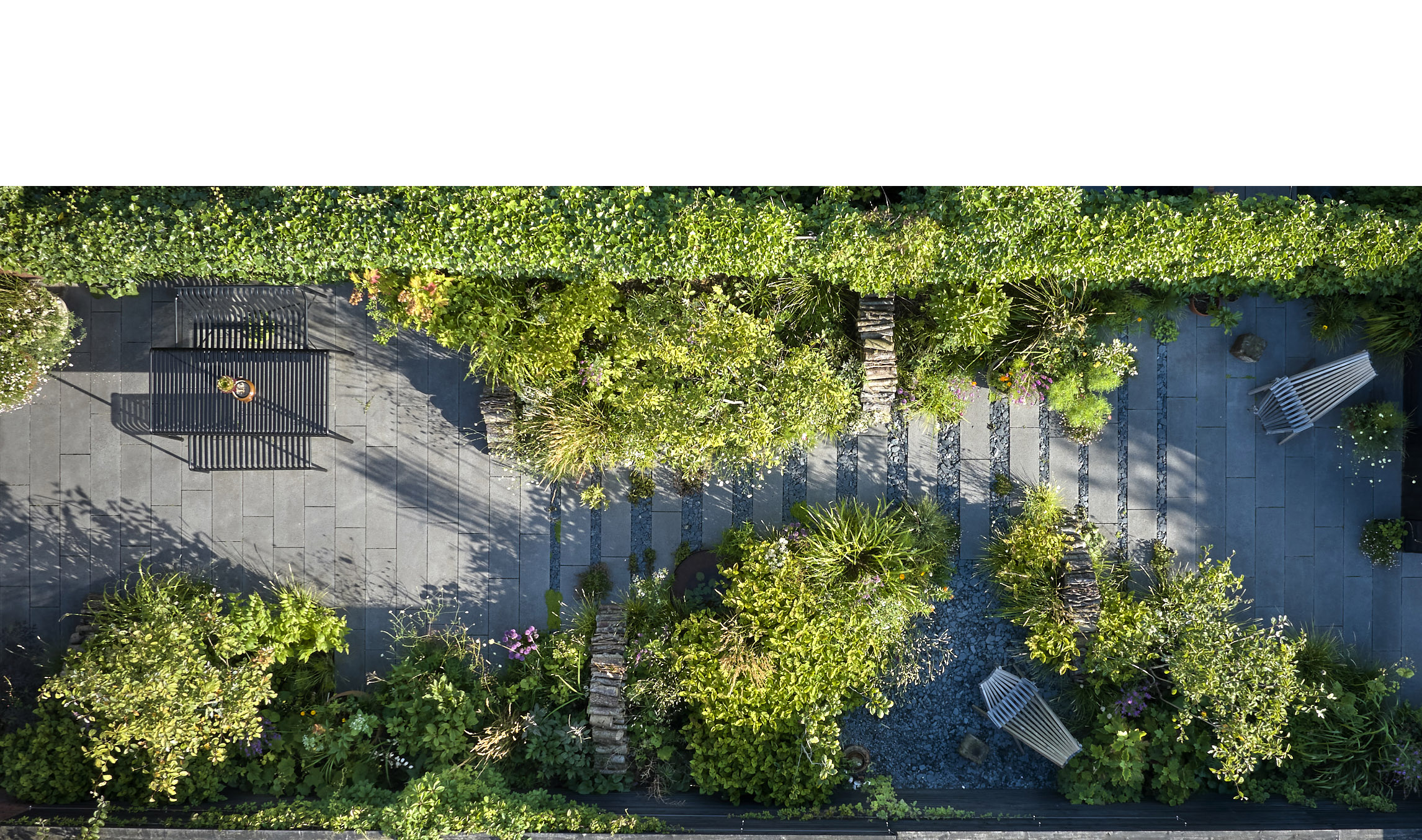 Fra denne vinkel ser man de mange fine designløsninger. Haven er delt op i 3 dele med terrassen nærmest huset (tv.), midterdelen er stort set fyldt ud med planter, og for enden ned mod haveskuret er der endnu en siddeplads. Bemærk også de markante brændestabler, der arkitektonisk skærer igennem beplantningen. Foto Alister Thorpe.