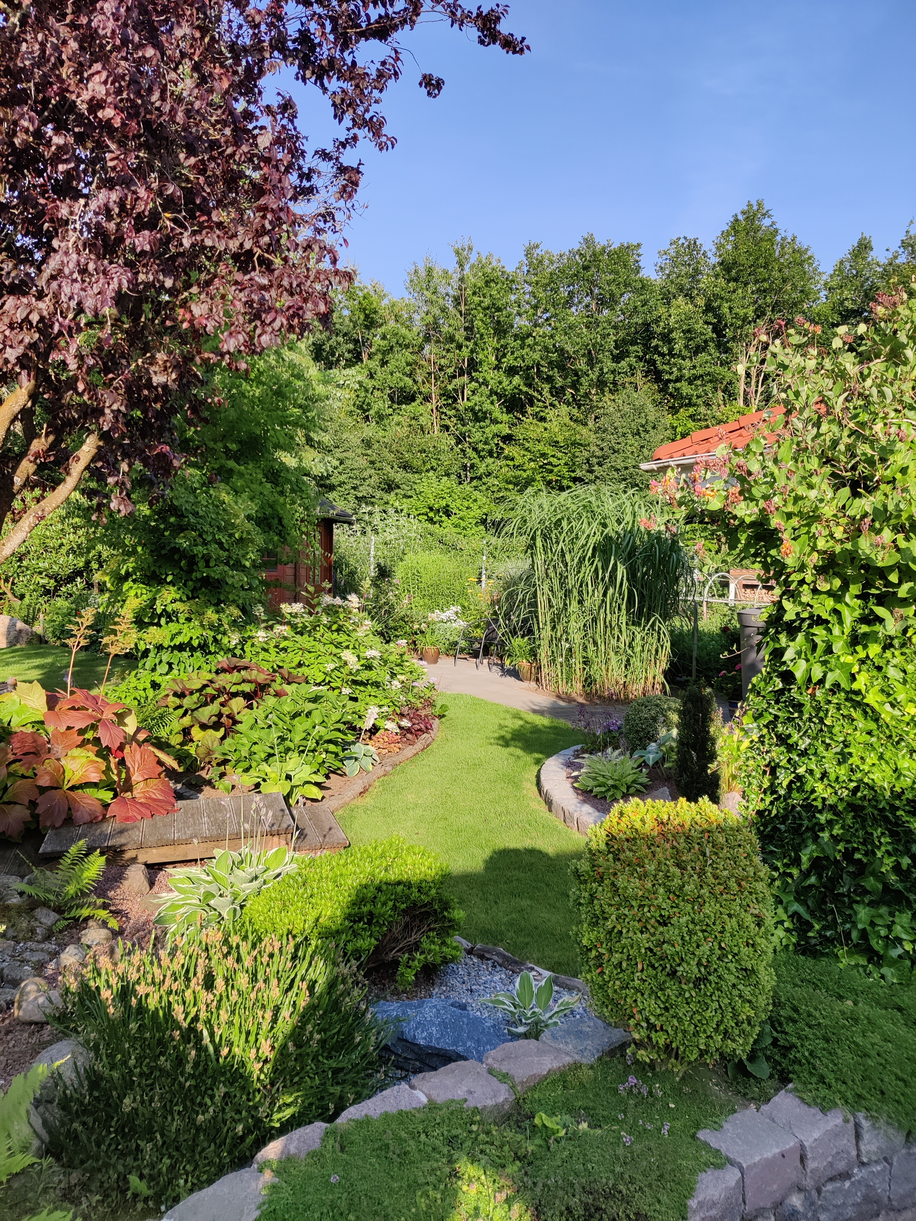 Havedesign med sten, træer, buske, terrasser og bede