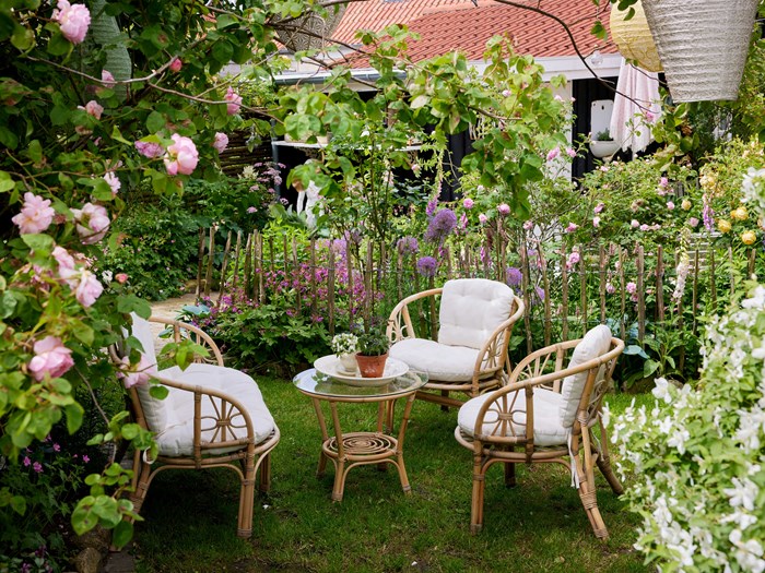 På en lille grøn plet i haven er der sat møblement op, og gennem et let kastanjehegn har man kig ind til et bed med roser, prydløg, fingerbøl, hostaer mm. Foto: Thomas Evaldsen